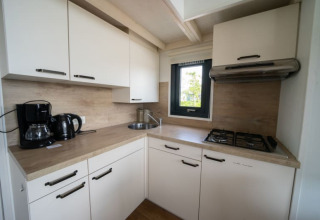 Cocina compacta de lodge con gabinetes blancos, estufa de gas, cafetera y pequeña ventana iluminada.