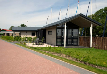 Photo de lodges modernes avec terrasse, mobilier d'extérieur, verdure et mâts de voiliers en arrière-plan.