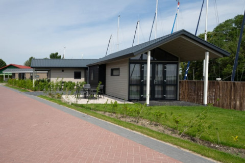 Foto van moderne lodges met een terras, tuinmeubilair, groen en duidelijk zichtbare zeilmasten op de achtergrond.