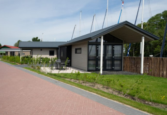 Et foto af moderne lodges med terrasse og udendørs siddeplads, omgivet af grønne planter og både i baggrunden.