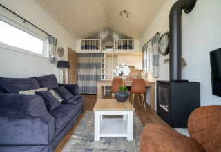 Salón moderno de lodge con sofá cómodo, mesa de comedor, chimenea, cama alta y decoración luminosa.