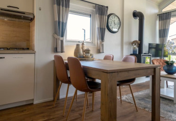 Intérieur de lodge moderne avec table en bois, quatre chaises, grande horloge, poêle et décoration chaleureuse.