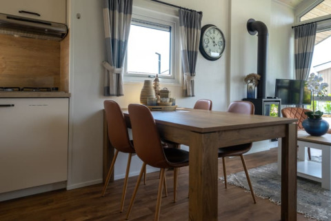 Moderne lodge met houten eettafel, vier stoelen, groot horloge, houtkachel, tv en gezellige inrichting.