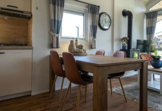Moderne lodge met houten eettafel, vier stoelen, groot horloge, houtkachel, tv en gezellige inrichting.