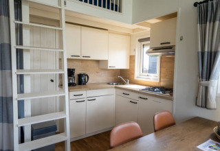 Moderne lodgekeuken met een ladder naar de slaapzolder, eettafel, gaskookplaat en koffiezetapparaat.
