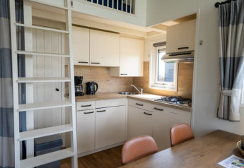 Moderne lodgekøkken med stige til hems, spisebord, gaskomfur, kaffemaskine og store vinduer.