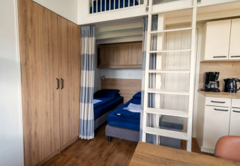 Chambre de lodge avec lits superposés, armoire en bois, coin cuisine, cafetière et bouilloire.
