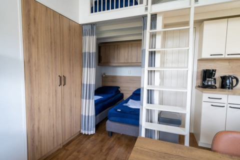 Lodgekamer met stapelbedden, houten kast, kitchenette, koffiezetapparaat en waterkoker op het aanrecht.
