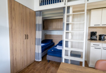 Lodgekamer met stapelbed, houten kast, kitchenette met koffiezetapparaat en waterkoker op het aanrecht.
