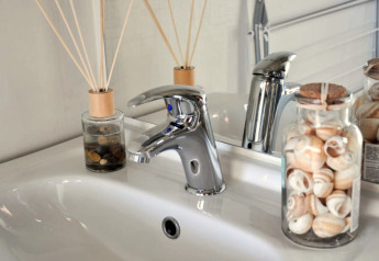 Vasque moderne dans un lodge, robinet chrome, pots de coquillages et bâtonnets parfumés sur le comptoir.
