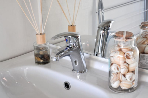 Vasque moderne dans un lodge, robinet chrome, pots de coquillages et bâtonnets parfumés sur le comptoir.