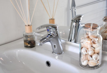 Zona de lavabo moderna en lodge con grifo cromado, frasco de conchas y varillas aromáticas decorativas.