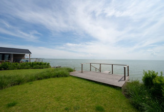 Vista di un lodge sul mare con una terrazza in legno, prato verde e cielo ampio con nuvole leggere.