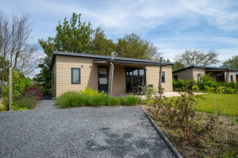 Moderne lodge met houten gevel, overdekte veranda en tuin, gelegen in een groene en rustige omgeving.