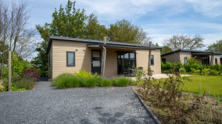 Moderne lodge med træfacade og veranda, omgivet af have og grønne områder under blå himmel.
