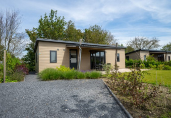 Moderne lodge med træfacade og veranda, omgivet af have og grønne områder under blå himmel.