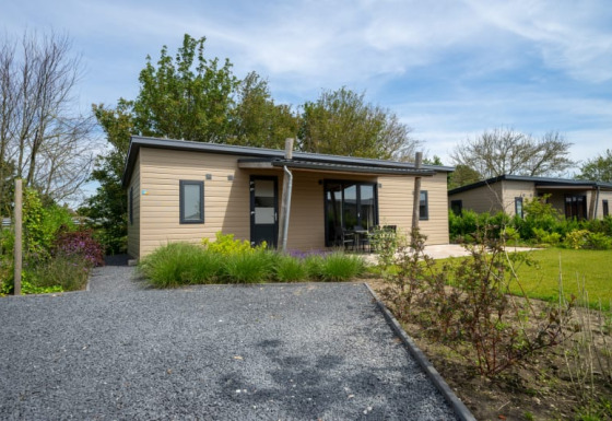 Moderne lodge med træfacade og veranda, omgivet af have og grønne områder under blå himmel.
