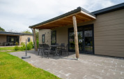 Outdoor area of a lodge with a covered patio, garden furniture, and green lawn on a bright sunny day.