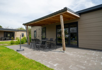 Espace extérieur d’un lodge avec terrasse couverte, mobilier de jardin et pelouse verte par une journée ensoleillée.