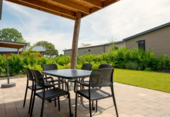 Terrasse extérieure couverte d'un lodge avec table et chaises, entourée de verdure et de bâtiments bas.