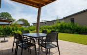Covered outdoor patio at a lodge with a table and chairs on stone tiles, overlooking lawns and cabins.