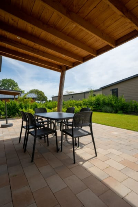 Covered outdoor patio at a lodge with a table and chairs on stone tiles, overlooking lawns and cabins.