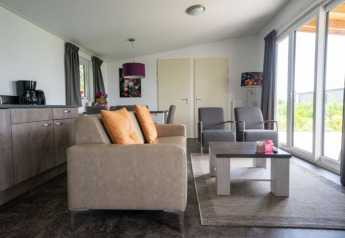 Salon moderne dans un lodge avec canapé, fauteuils, table basse et grandes fenêtres donnant sur la verdure.