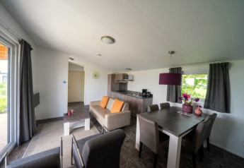 Intérieur de lodge lumineux et moderne avec canapé, table à manger, cuisine et grandes fenêtres à rideaux gris.