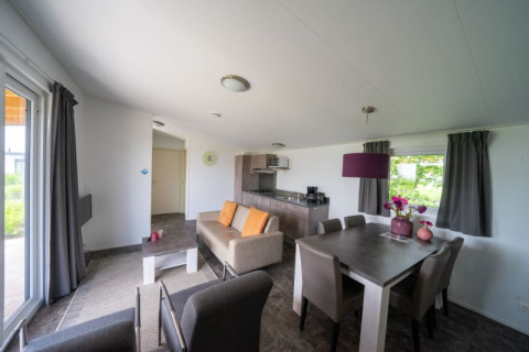 Bright, modern lodge interior featuring a sofa, dining table, kitchen, and large windows with gray curtains.