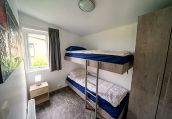 Petite chambre d'une lodge avec lits superposés, table de chevet, fenêtre, armoire et tableau mural visible.