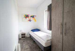 Camera da letto moderna e semplice in un lodge con letto singolo, armadio, tavolino e arte colorata.