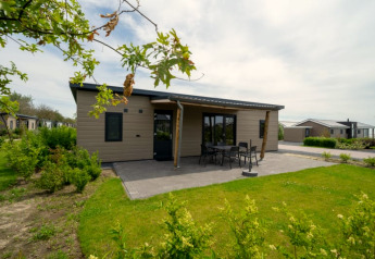 Lodge confortable avec terrasse et mobilier de jardin, entourée de verdure dans un parc de vacances paisible.