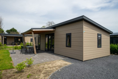 Moderna lodge con tetto piano, patio e mobili da giardino, situata in un contesto naturale e tranquillo.