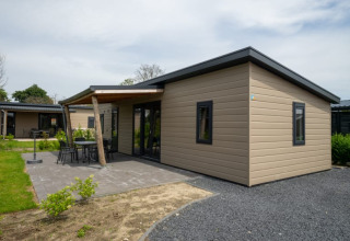 Moderne lodge med fladt tag, udendørs terrasse og havemøbler, beliggende i grønne omgivelser.