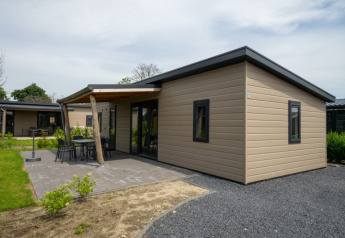 Moderna lodge con tetto piano, patio e mobili da giardino, situata in un contesto naturale e tranquillo.