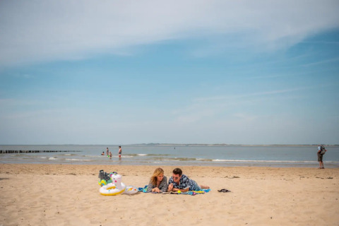 Twee mensen ontspannen op een strand tijdens een zonnige dag, vlakbij een glamping vakantiepark aan zee.
