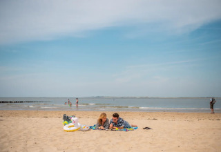 Twee mensen ontspannen op een strand tijdens een zonnige dag, vlakbij een glamping vakantiepark aan zee.
