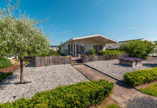 Modern vakantiepark met glamping accommodatie, grindtuin, houten paden, bloemen en groene struiken.