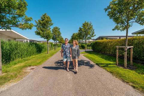 Koppel wandelt op een zonnige dag door een vakantiepark met glamping accommodaties en groene tuinen.