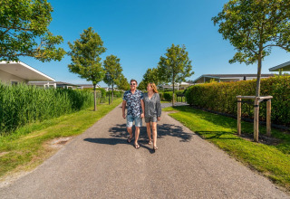 Koppel wandelt op een zonnige dag door een vakantiepark met glamping accommodaties en groene tuinen.