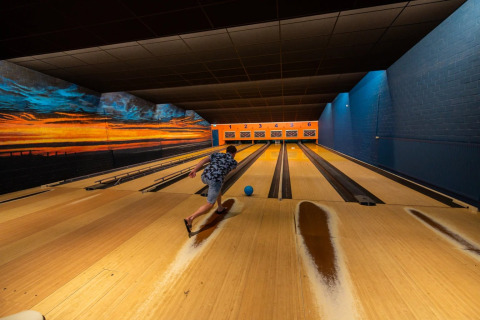 Persoon gooit een bowlingbal in een kleurrijk verlichte indoor bowlingbaan bij een vakantiepark met glamping.