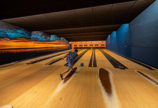 Persoon gooit een bowlingbal in een kleurrijk verlichte indoor bowlingbaan bij een vakantiepark met glamping.