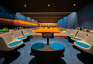 Een moderne bowlingbaan in een vakantiepark, gezien vanaf het zitgedeelte met kleurrijke stoelen.