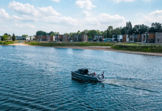 Een boot vaart op het water langs een vakantiepark met luxe glamping accommodaties aan de oever.