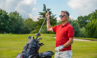 Man in rode polo op een golfbaan, haalt een golfclub uit tas, omringd door groen en zonnig weer.