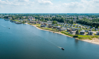 Luchtfoto van een vakantiepark aan het water met moderne glamping accommodaties en groene omgeving.