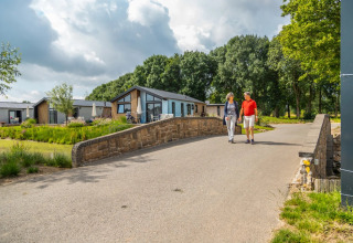 Koppel wandelt over brug bij moderne glampingaccommodaties in een groene omgeving van een vakantiepark.