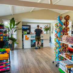 Vakantiepark receptie met speelgoed, snacks en drankjes, man bij balie, glamping accommodatie mogelijk.