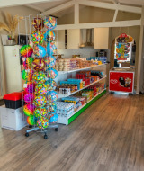 Interieur van een kleine winkel in een vakantiepark met snacks, dranken, ijs en kleurrijke strandballen.