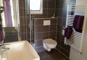 Moderne badkamer in een lodge met hangtoilet, glazen douchecabine, wastafel en handdoekradiator.